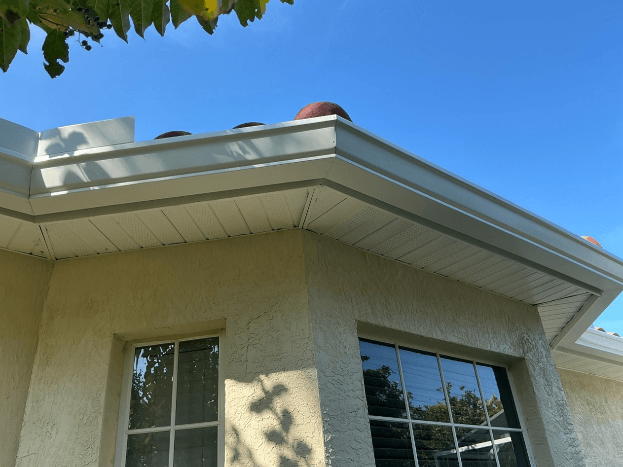 A view of new white gutters on a beige stucco house from below.